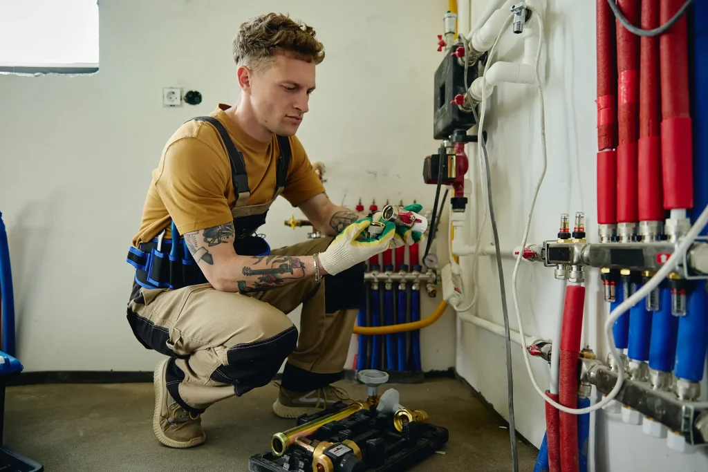 Heizungsmonteur mit Arbeitshandschuhen bei der Installation einer Heizungsanlage in einem Technikraum.