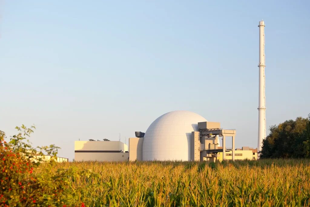 Kernkraftwerk mit Kuppelgebäude und hohem Schornstein hinter einem Maisfeld.